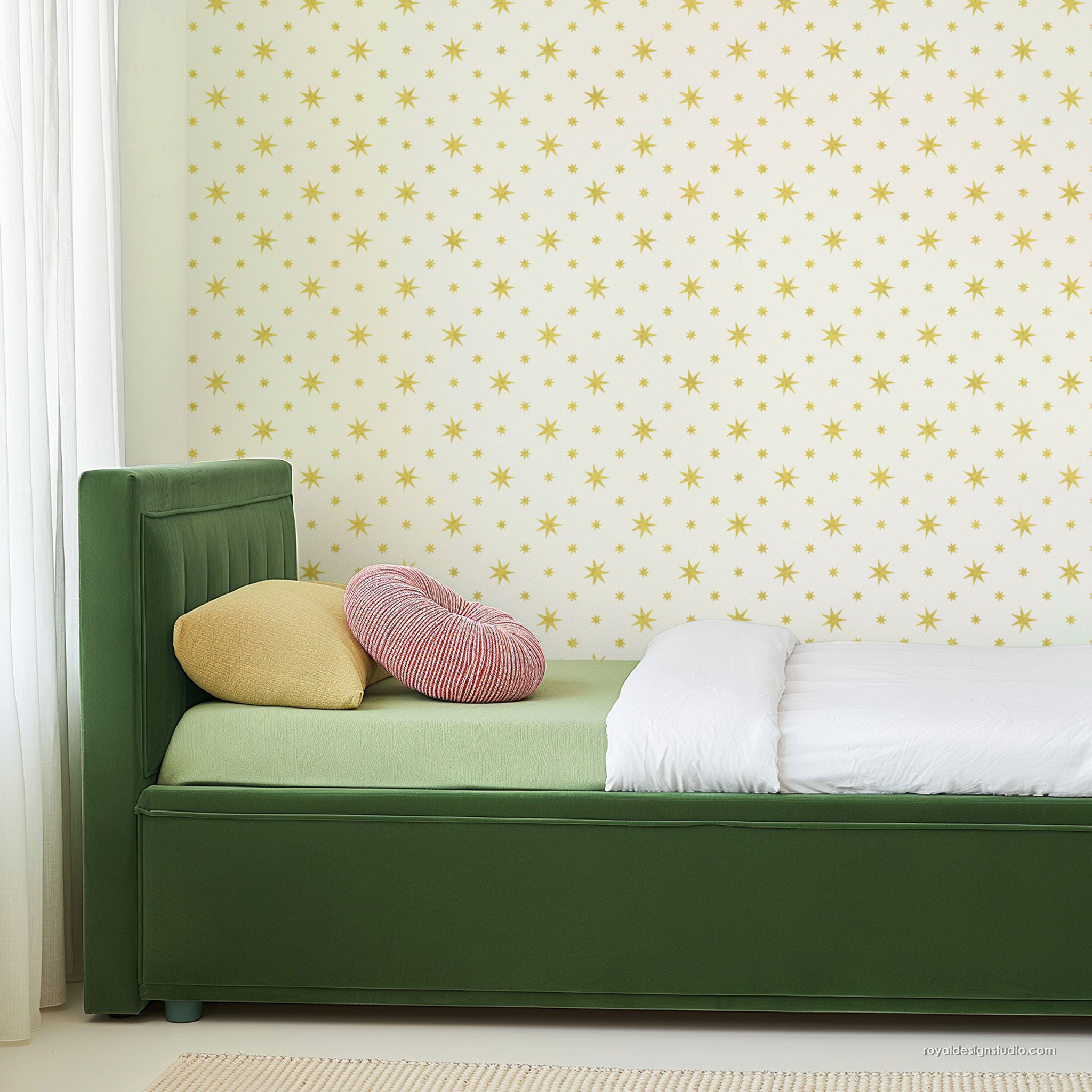 A green upholstered bed frame with a light green mattress, white folded bedding, a yellow pillow, and a pink striped pillow, set against a cream wall with yellow starburst design.
