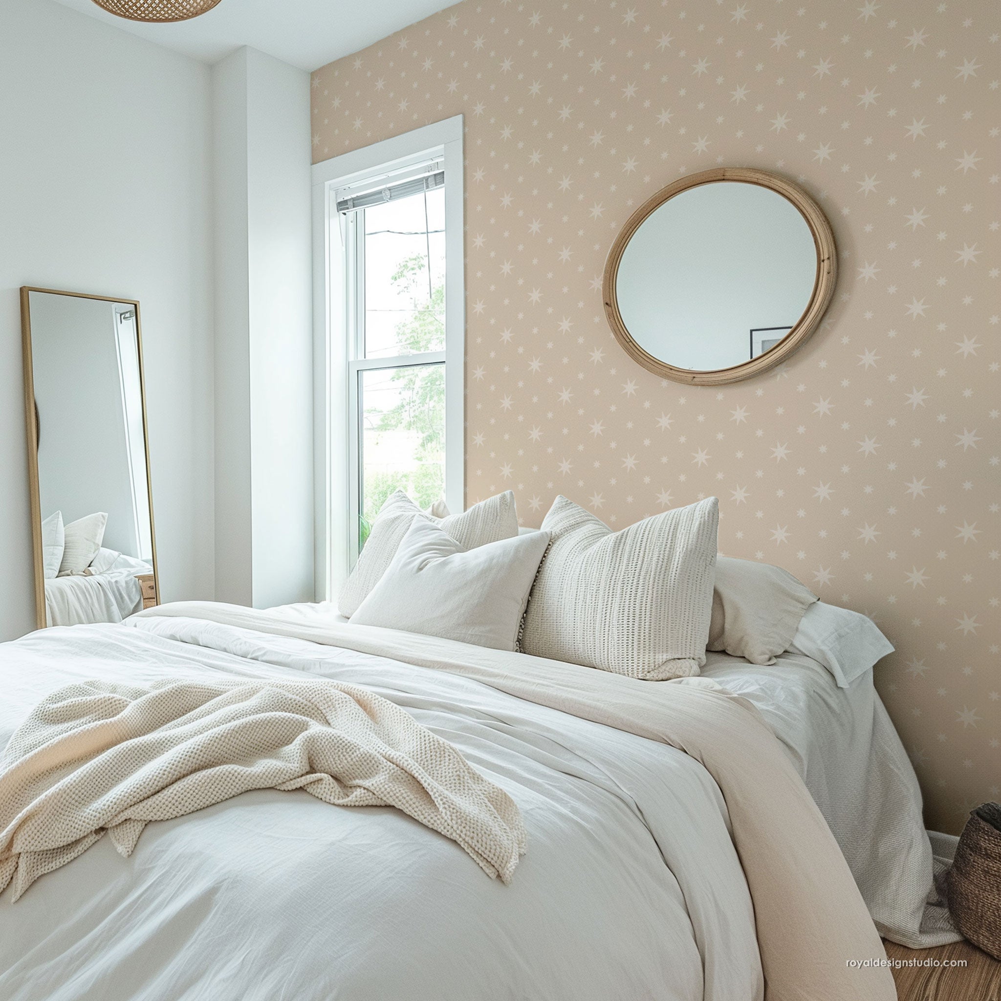 A styled bedroom interior featuring a bed dressed in white bedding and a cream throw blanket, set against a wall with pale blush wall patterned with small white stars. A round wood-framed mirror hangs on the wall, and a tall floor mirror is visible on the left.