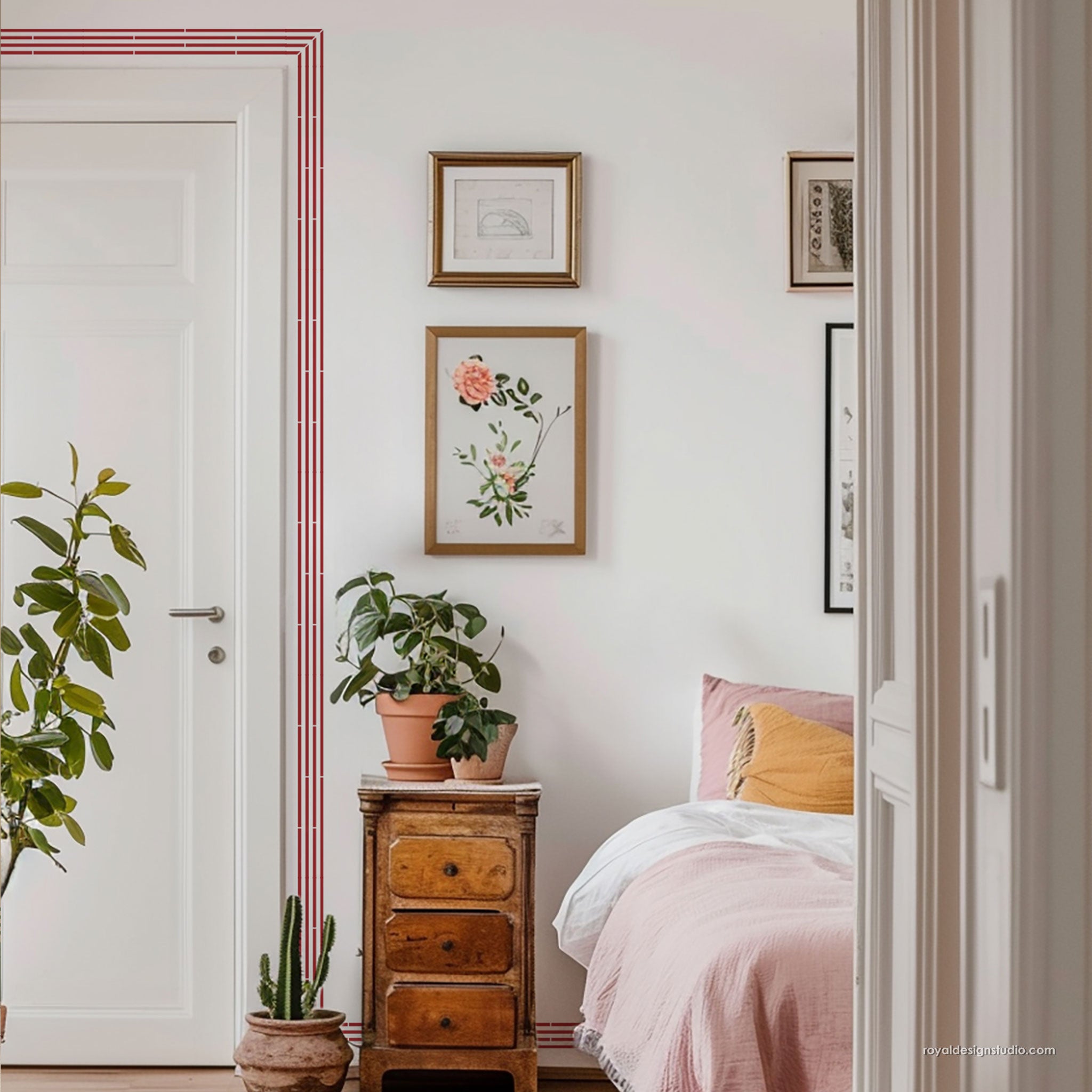 A styled bedroom interior with a pink bed, wooden nightstand, potted plants, framed wall art, and a white door with red trim in the background.