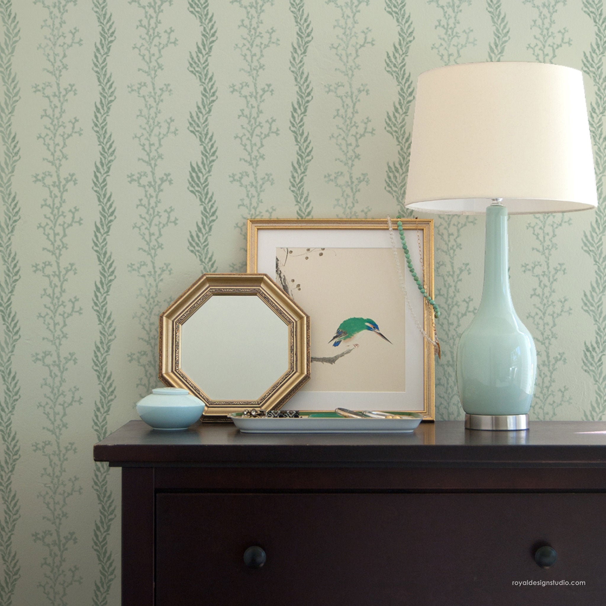Decorative items on a bedroom dresser against a coastal pattern wall stencil with coral motif