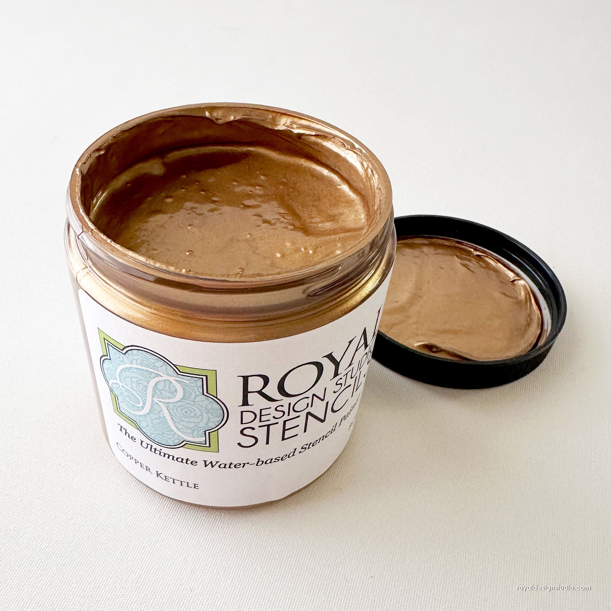 An open jar of Royal Design Studio Stencil 'Copper Kettle' showing the metallic copper-brown stencil paste inside, with its black lid resting beside it on a light off-white background.