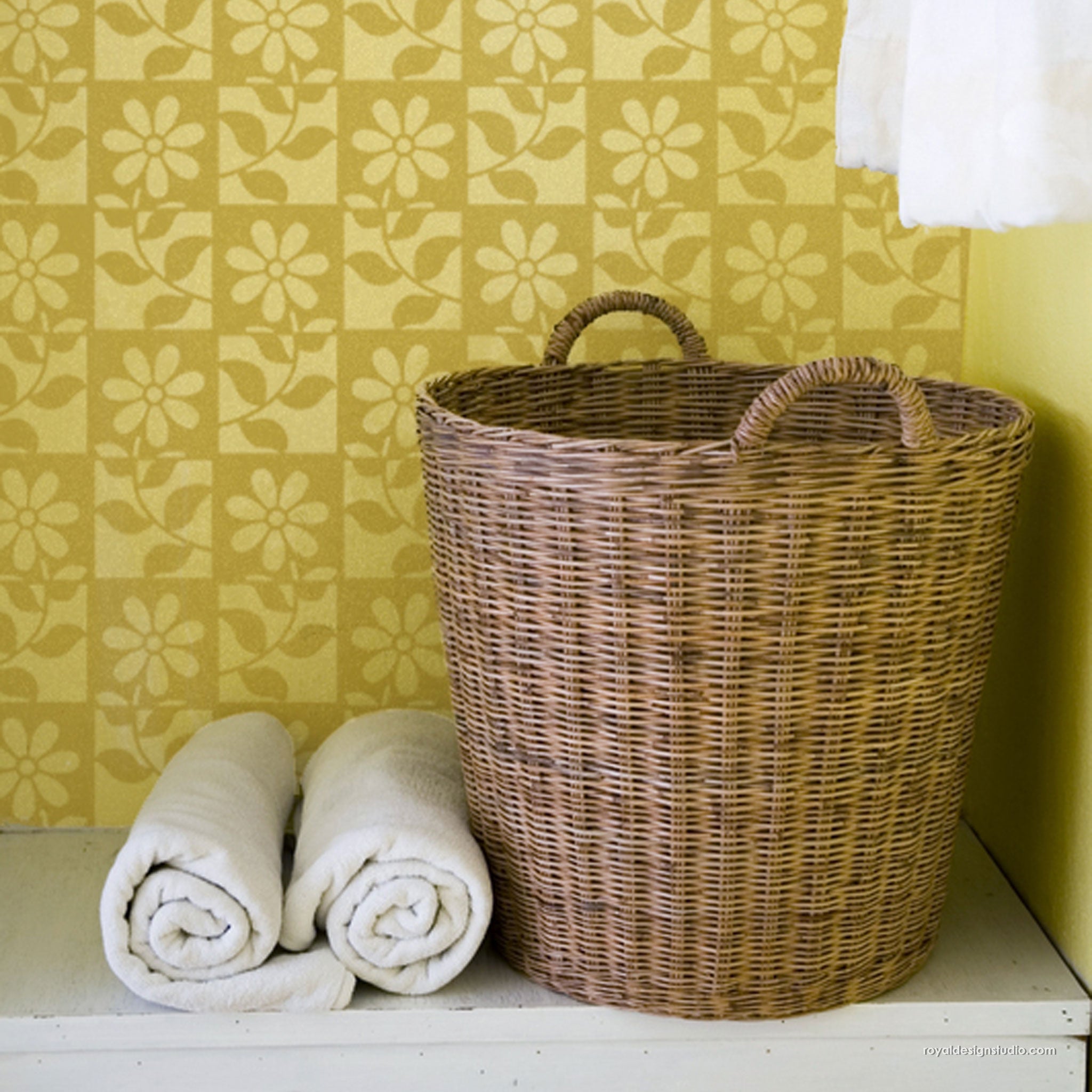 Wicker laundry basket with folded towels against a yellow floral-patterned wall stencil design.