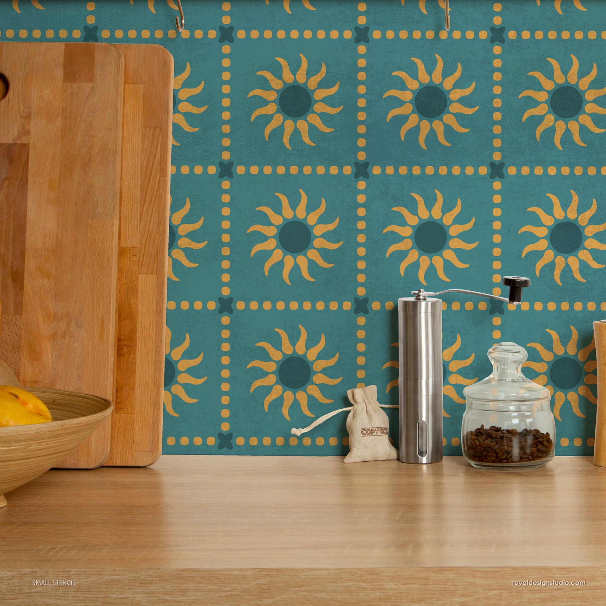 Kitchen counter with coffee grinder, jar of coffee beans, and wooden cutting board against a stenciled wall.
