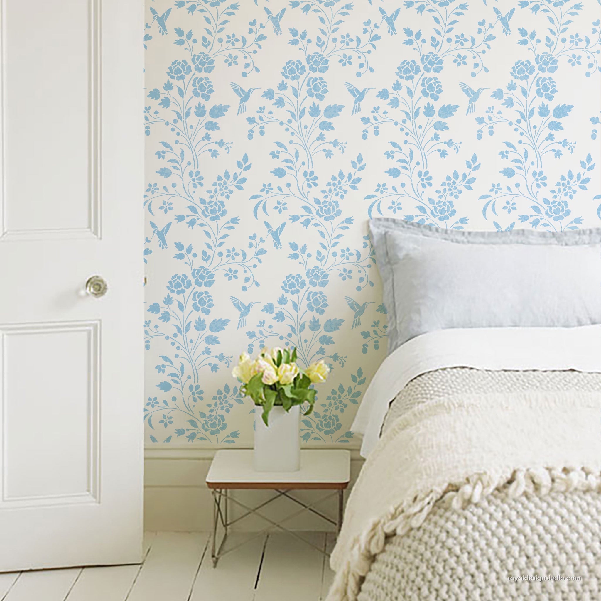 Bedroom with floral Chinoiserie stencil design painted on the wall with a cottage style  bed, and small table with flowers.