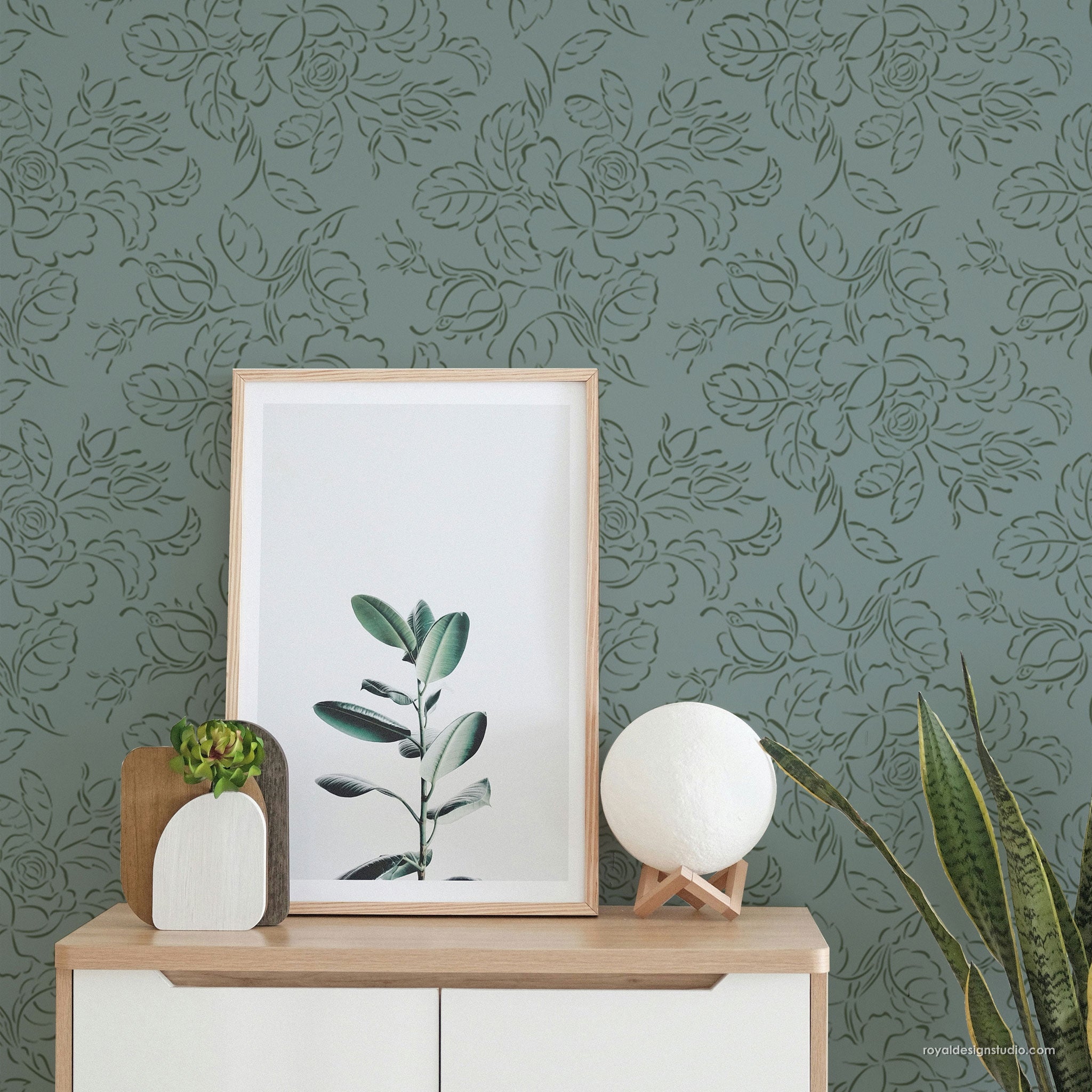 Framed plant print on a wooden shelf against a floral  stenciled wall.