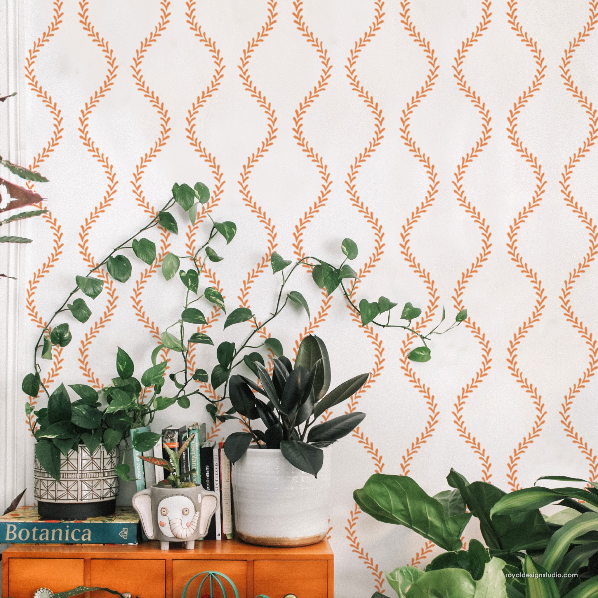 Room interior with plants and a cabinet against a wall with decorative orange and white trellis wall stencil pattern.