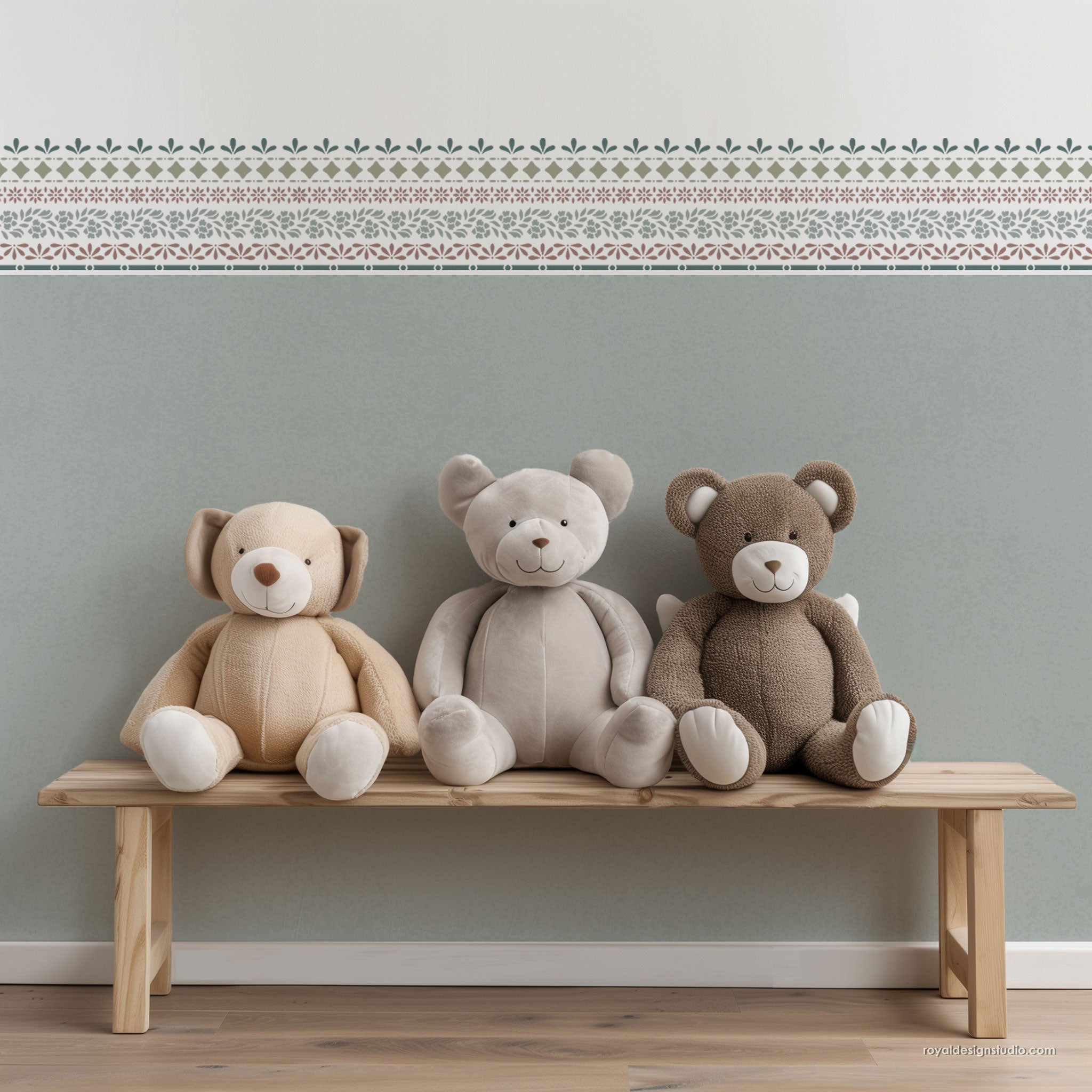 Three plush teddy bears in beige, cream, and brown sit on a light wood bench against a pale green wall with a decorative border pattern.