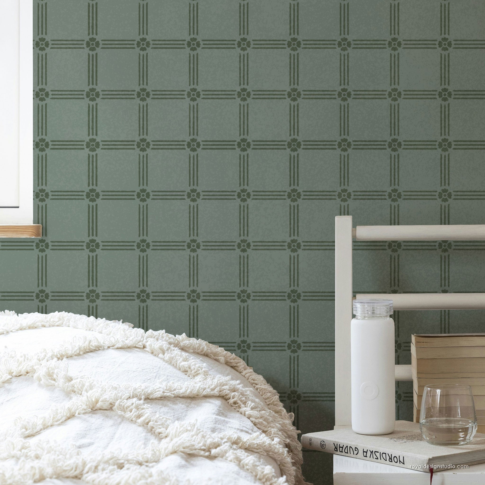 Green geometric patterned wall shown on a bedroom wall behind a bed with white bedding and a bedside table.