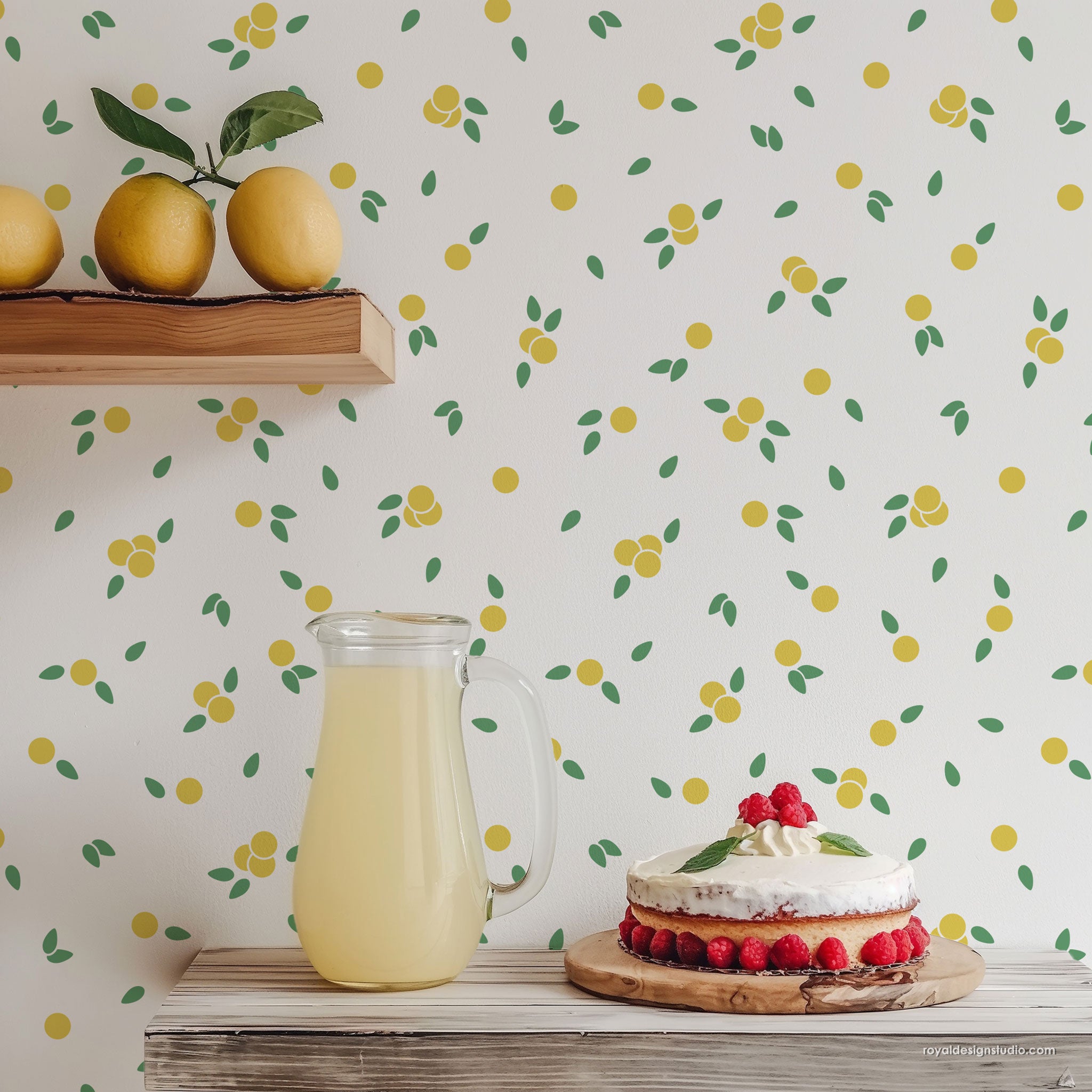 Lemon and green leaf patterned wall shown in a styled kitchen scene with a glass pitcher of lemonade and a layered cake on a wooden board.
