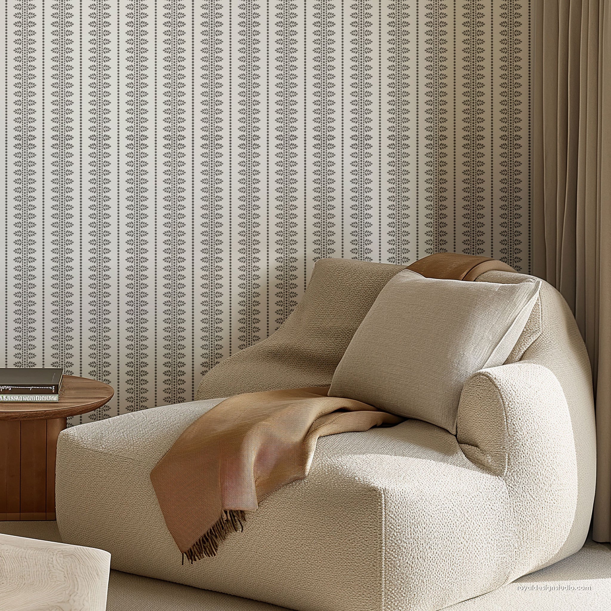A modern upholstered lounge chair in a warm cream bouclé fabric, styled with a tan throw blanket and a matching cushion, set against patterned wall and a wooden side table.