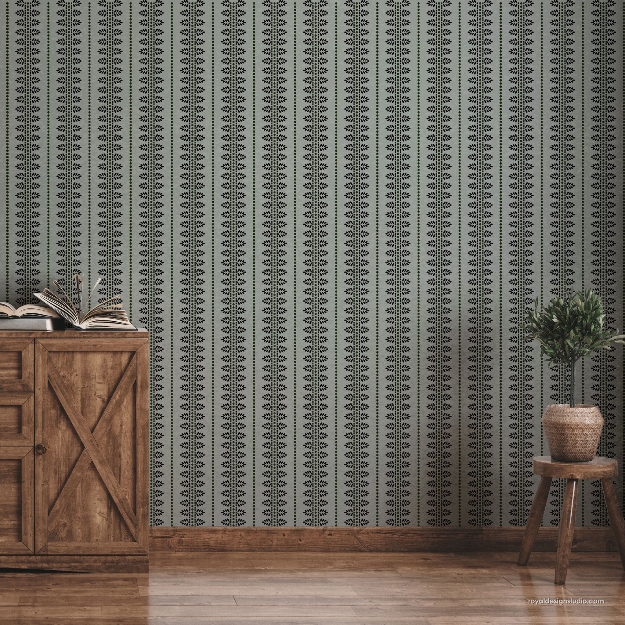 Vertical patterned wall in muted sage green and charcoal gray with a repeating geometric motif, shown in a styled room setting with a wooden cabinet, books, stool, and potted plant.