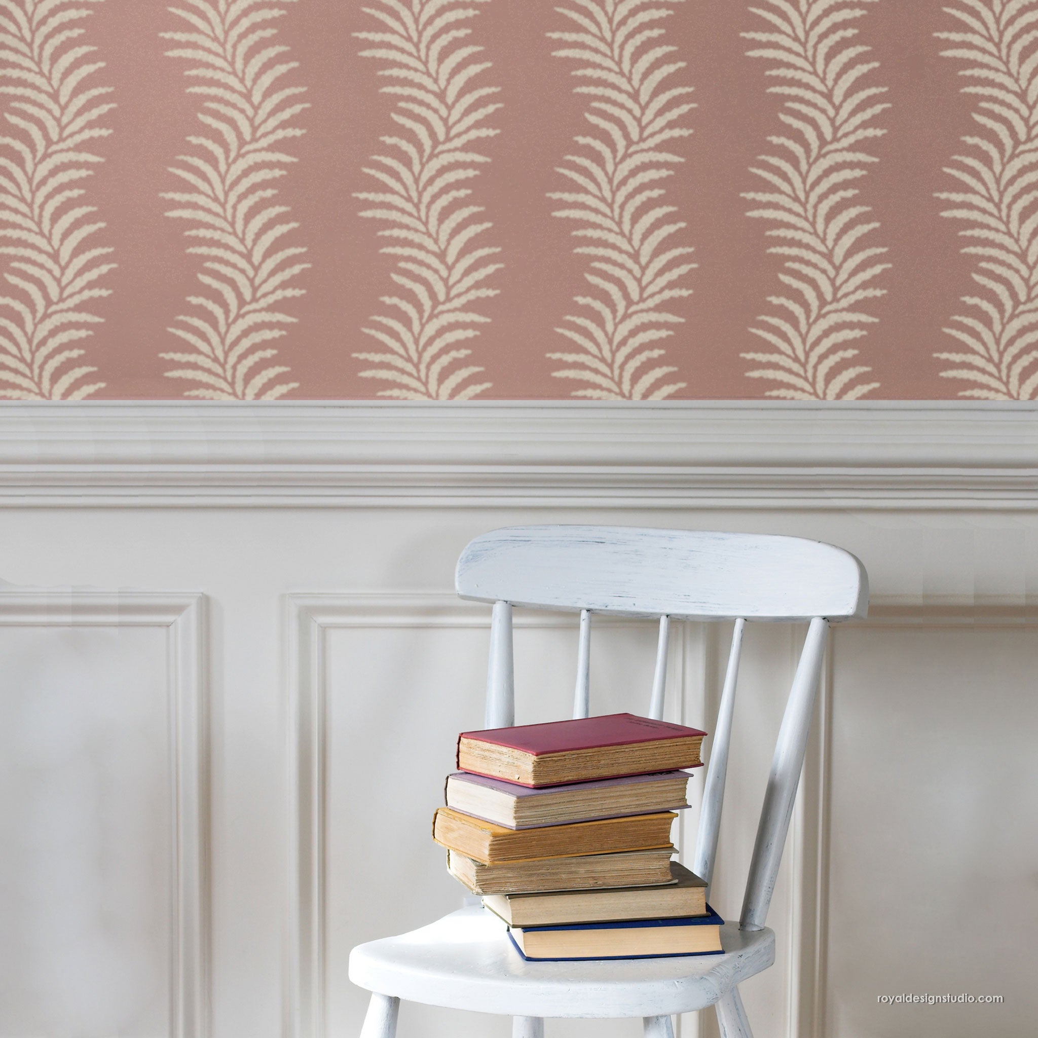 Stack of books on a white chair against a wall with a leaf pattern