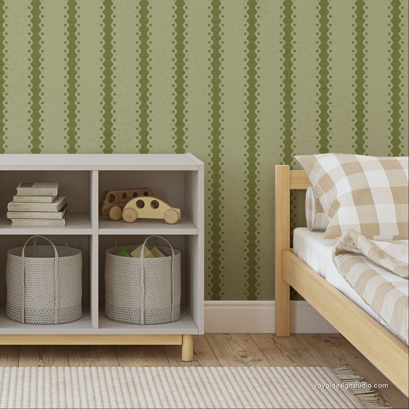 A styled children's bedroom corner featuring sage green wall with vertical dotted stripes, a light gray 3-compartment storage shelf with toys and gray baskets, and a wooden bed frame with a beige checkered pillow.